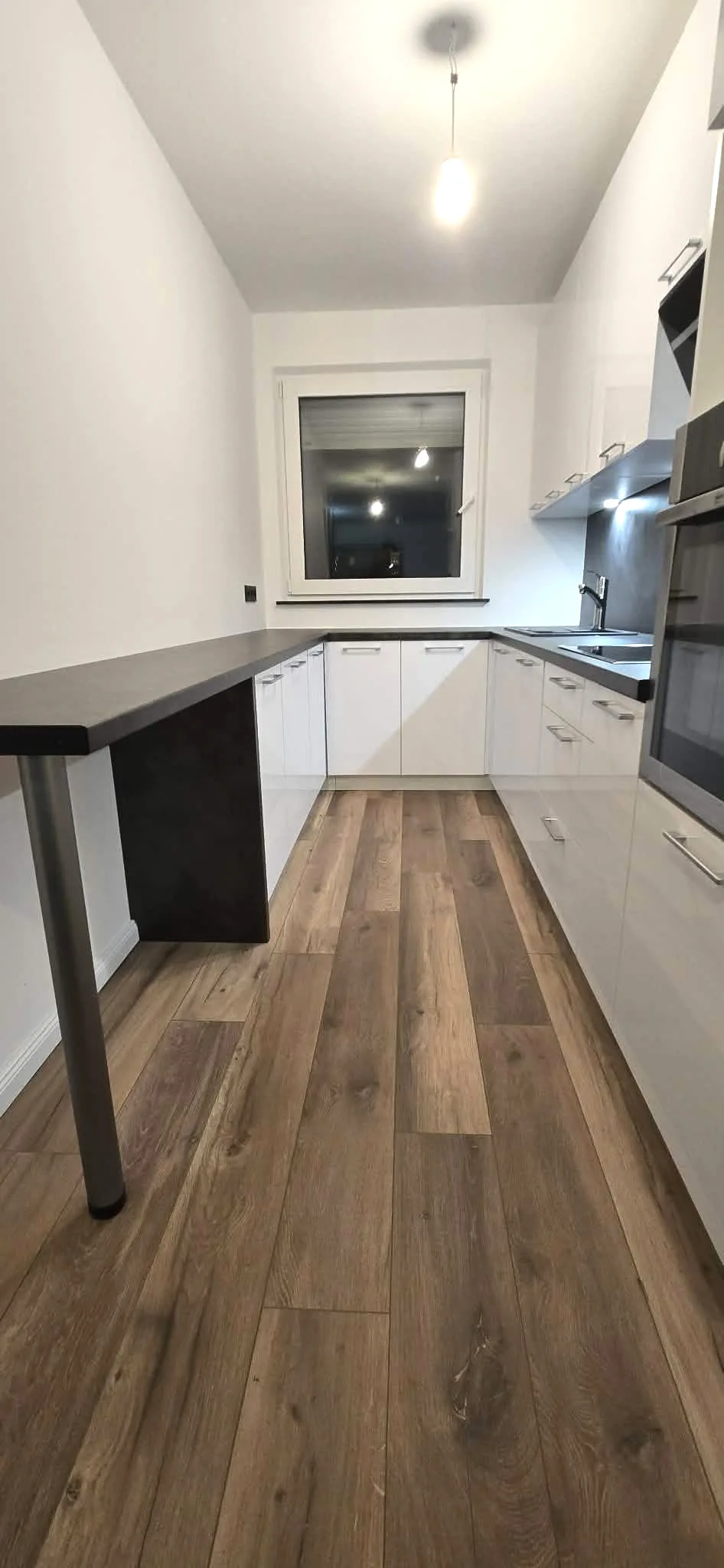 Weiße Küche mit dunkler Theke, Holzfußboden und eingebautem Backofen