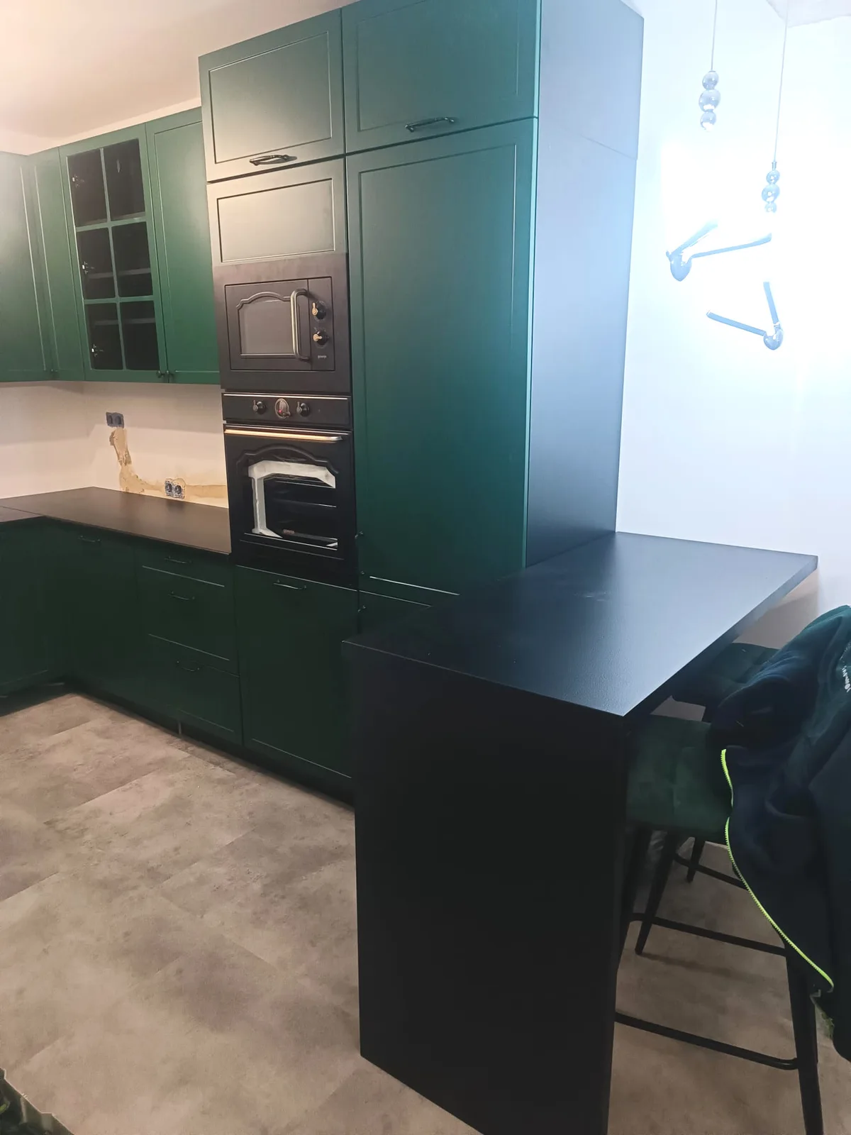 Dunkelgrüne Küche mit schwarzer Arbeitsplatte und Hochschrank mit Backofen