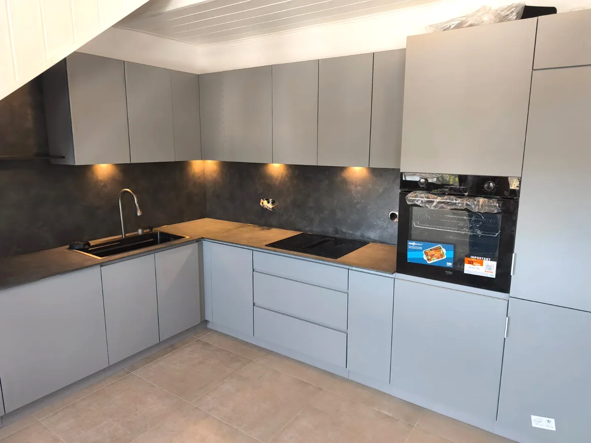 Graue Küche mit Holzarbeitsplatte, dunkler Rückwand und eingebautem Backofen