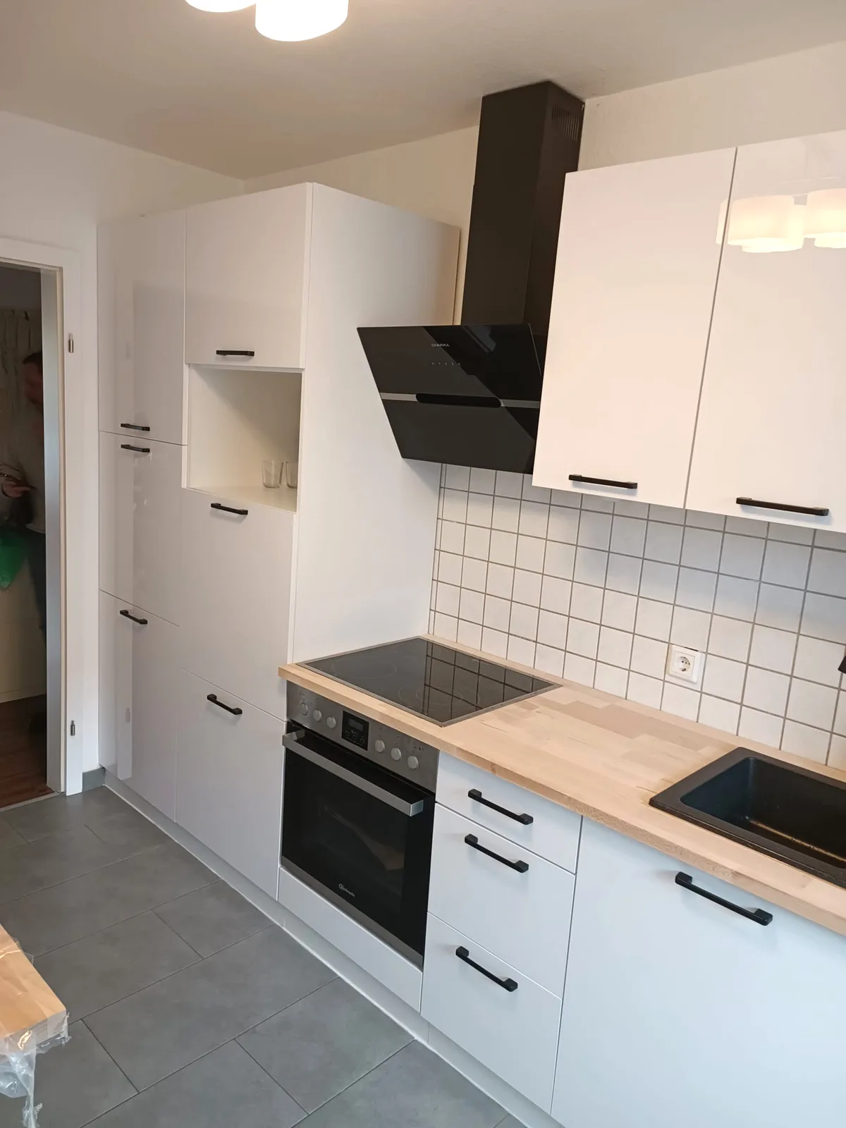 Kleine weiße Küche mit Holzarbeitsplatte, weißen Fliesen und Hochschrank