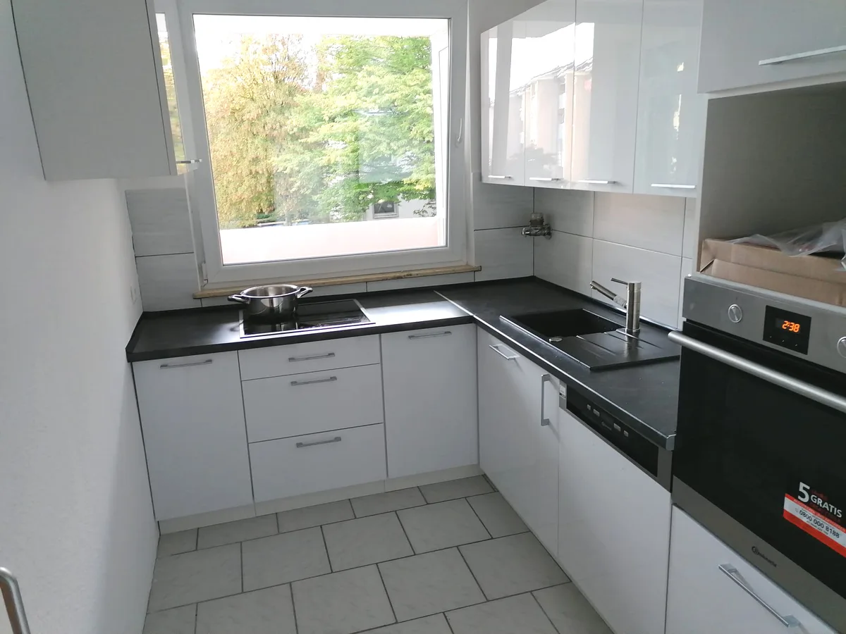 Helle Küche mit dunkler Arbeitsplatte, schwarzer Spüle und Eckfenster