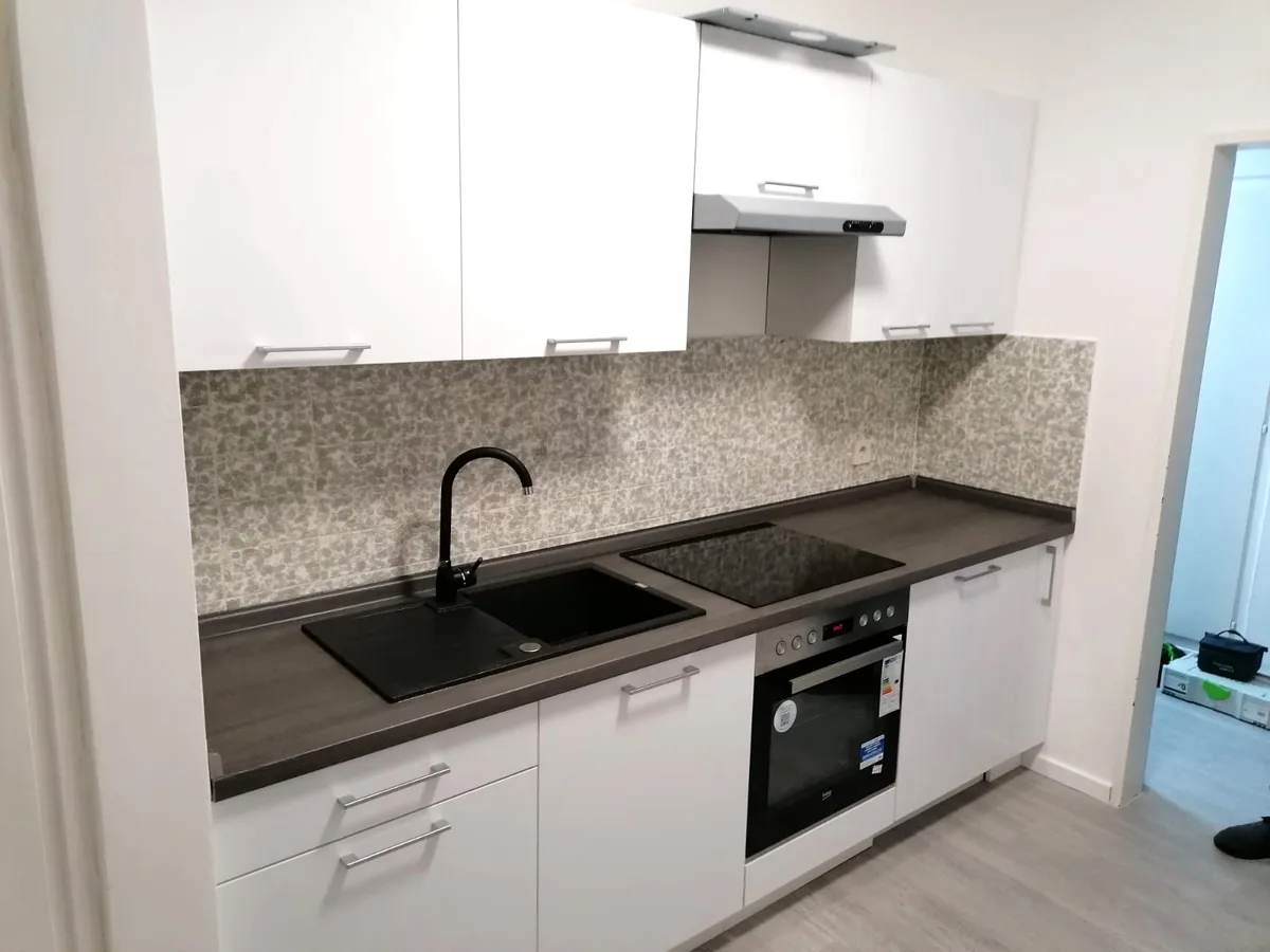 Weiße Küche mit Granitoptik-Arbeitsplatte, schwarzer Spüle und Backofen